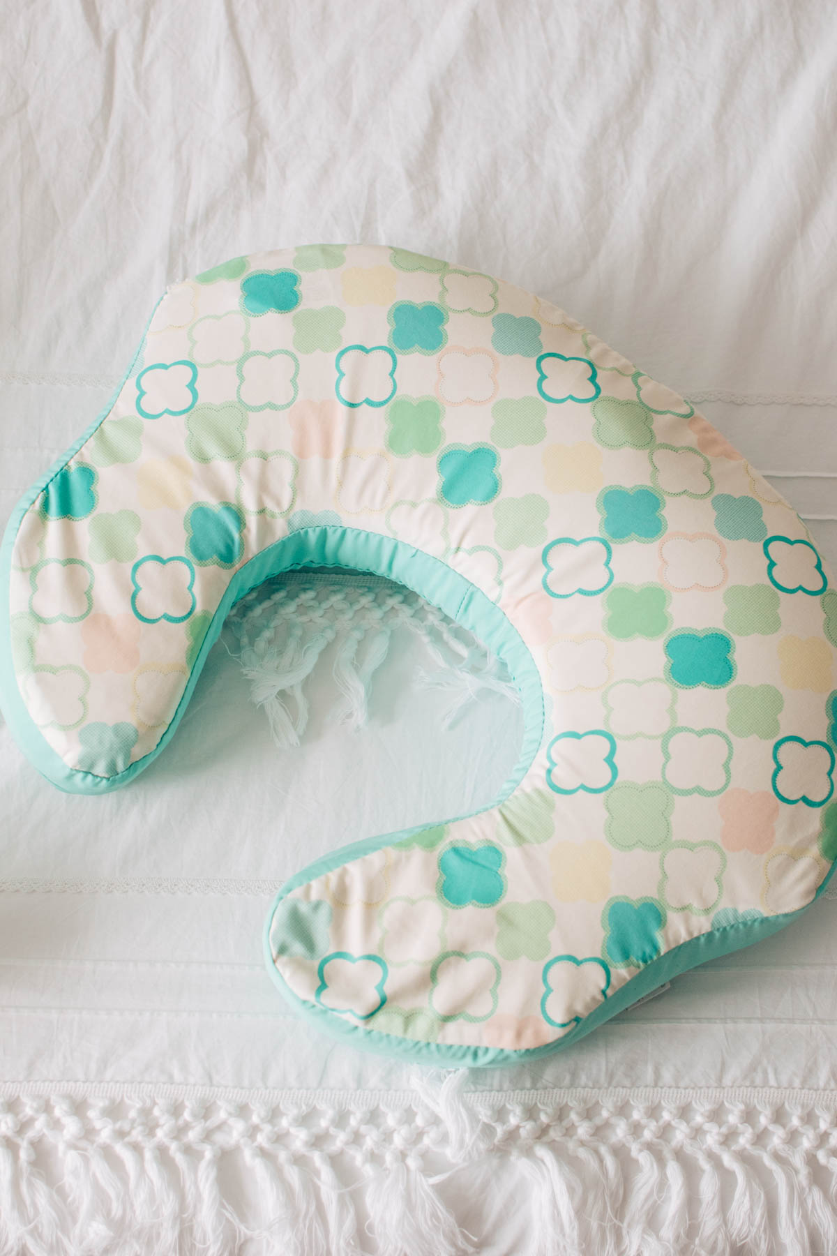 Nursing pillow with geometric pattern cover on white duvet cover.