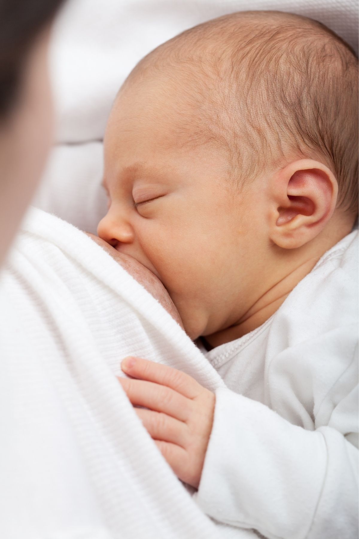 Newborn baby wearing white nurses with a proper latch with wide mouth and chin against breast.