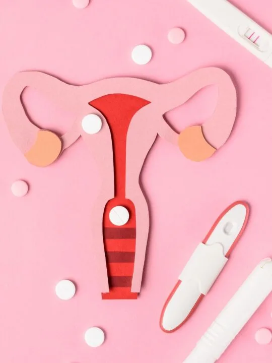 Diagram of uterus with implanted egg surrounded by several pregnancy tests on pink background.