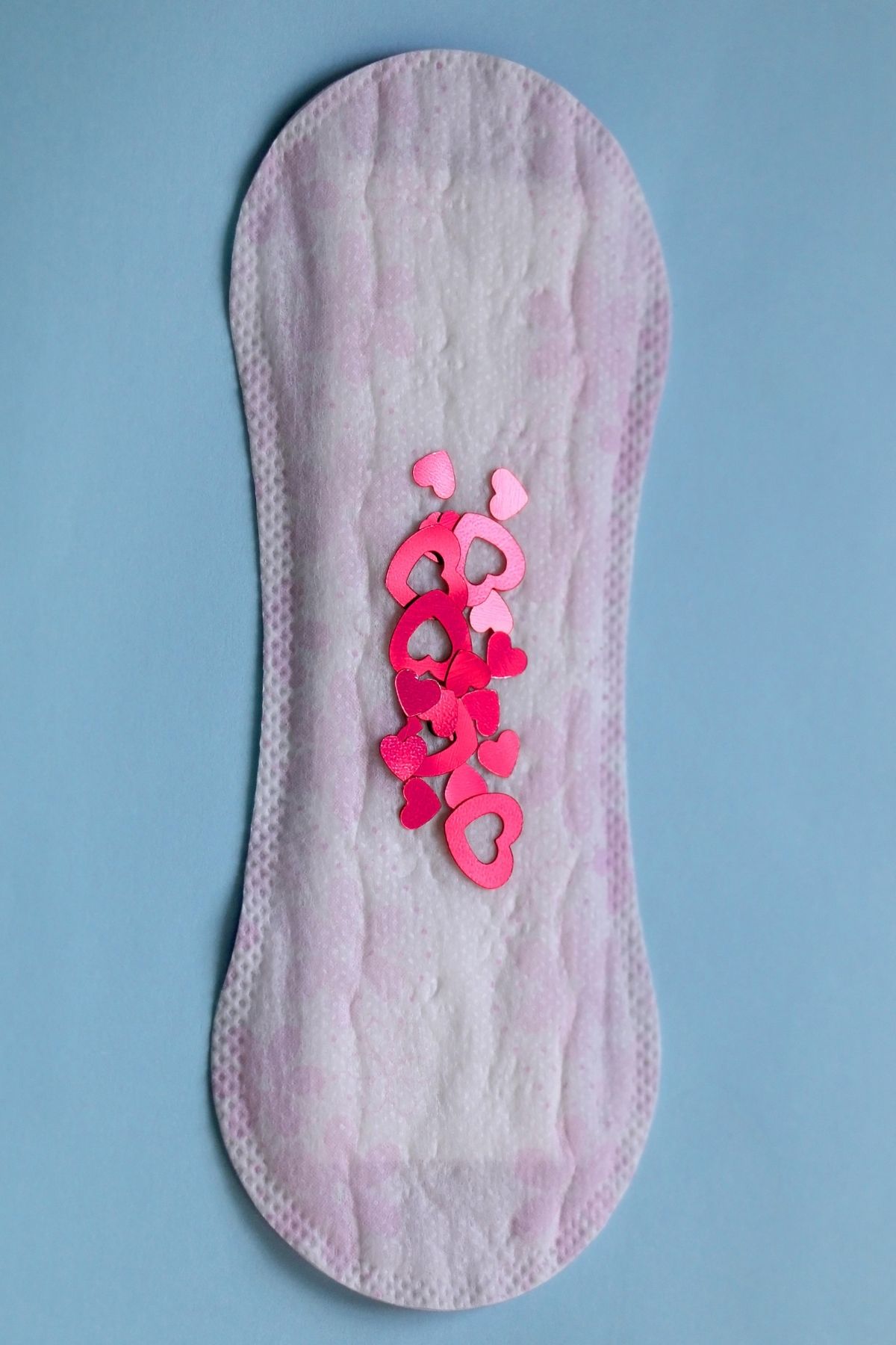 Small sanitary pad on blue background; pad has red confetti down middle to represent blood.