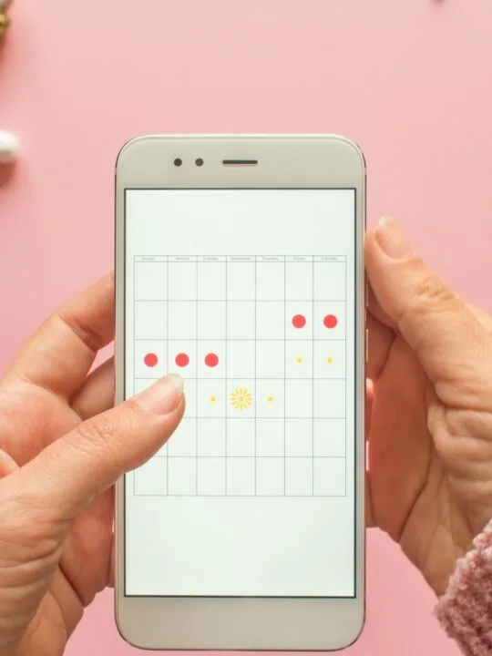 Woman holds phone with an app for tracking menstrual cycles using a calendar and dots.