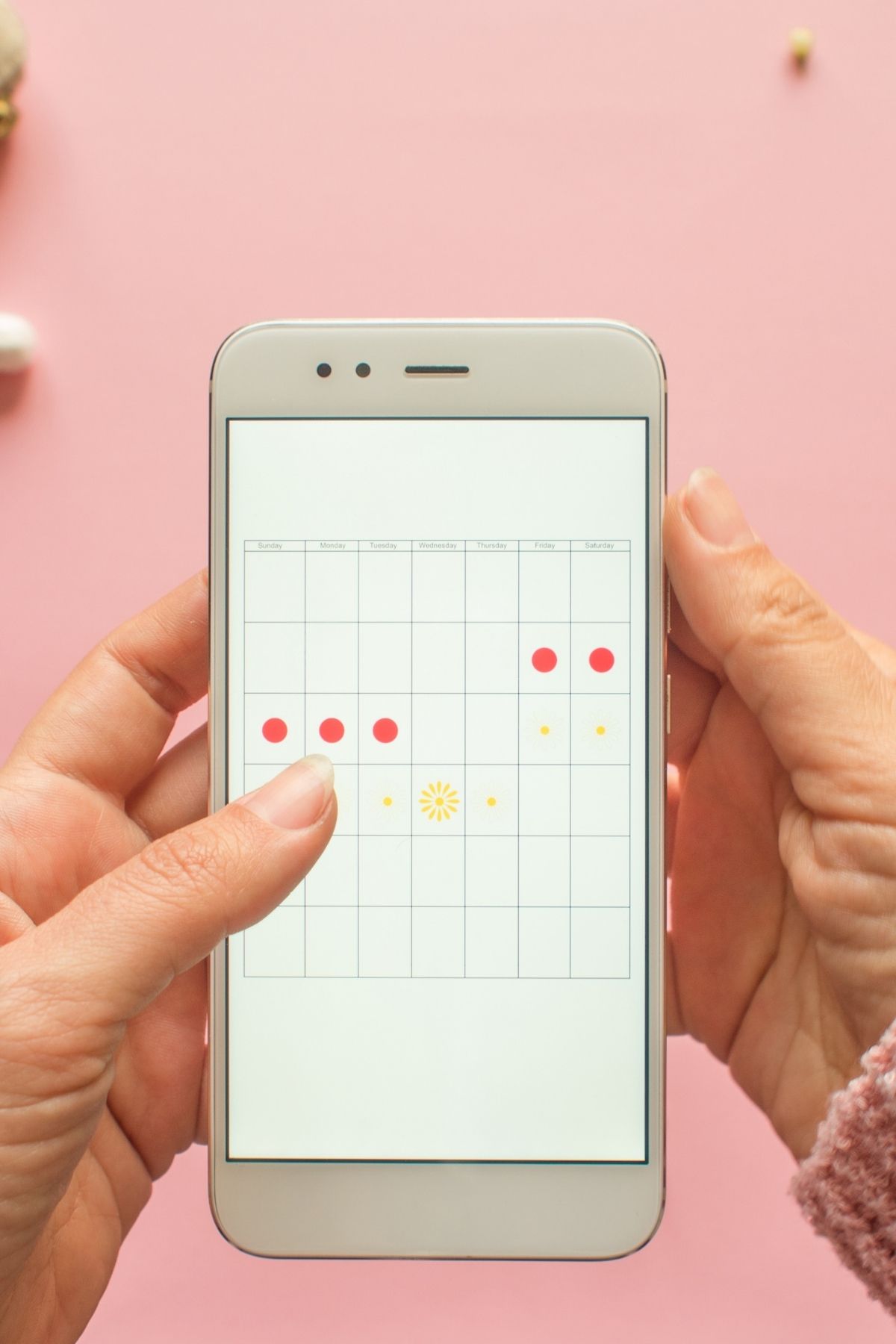 Woman holds phone with an app for tracking menstrual cycles using a calendar and dots.