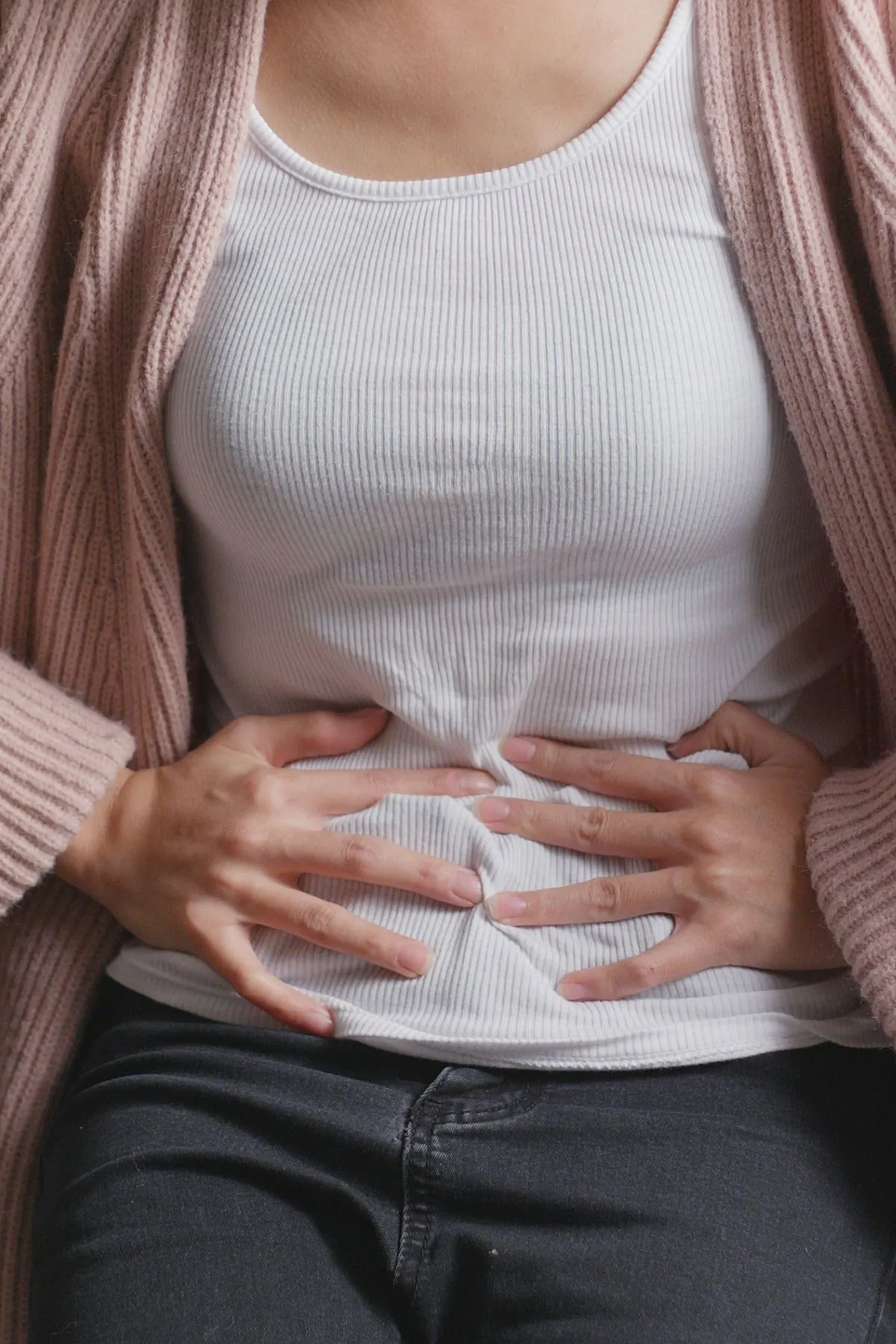 Woman hunches over and presses her hands to her stomach while experiencing abdominal pain.