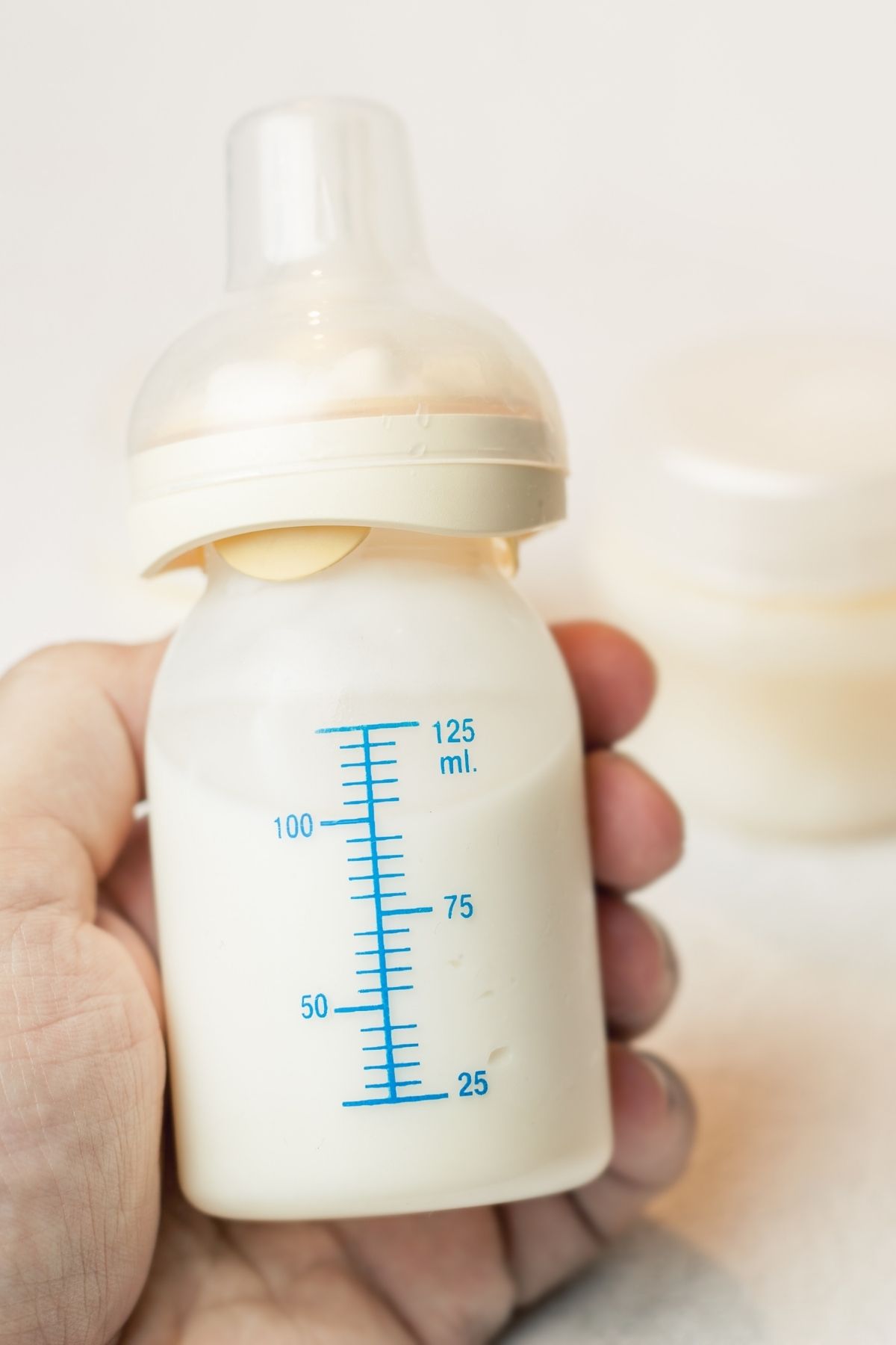 Woman holds small baby bottle with blue markings filled with breastmilk.