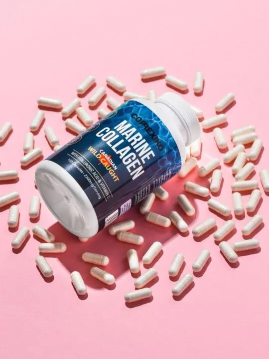 Bottle of marine collagen surrounded by loose collagen pills on pink background.