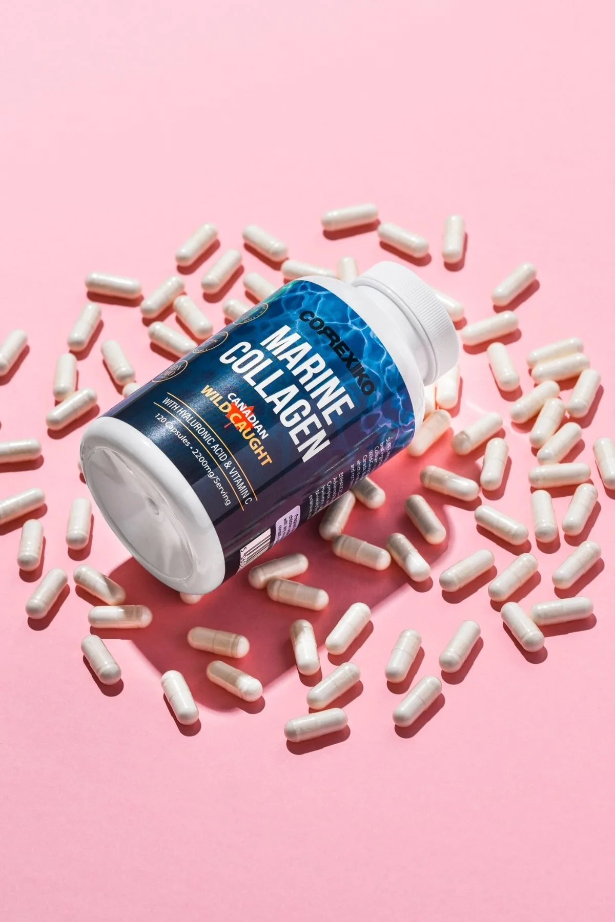 Bottle of marine collagen surrounded by loose collagen pills on pink background.