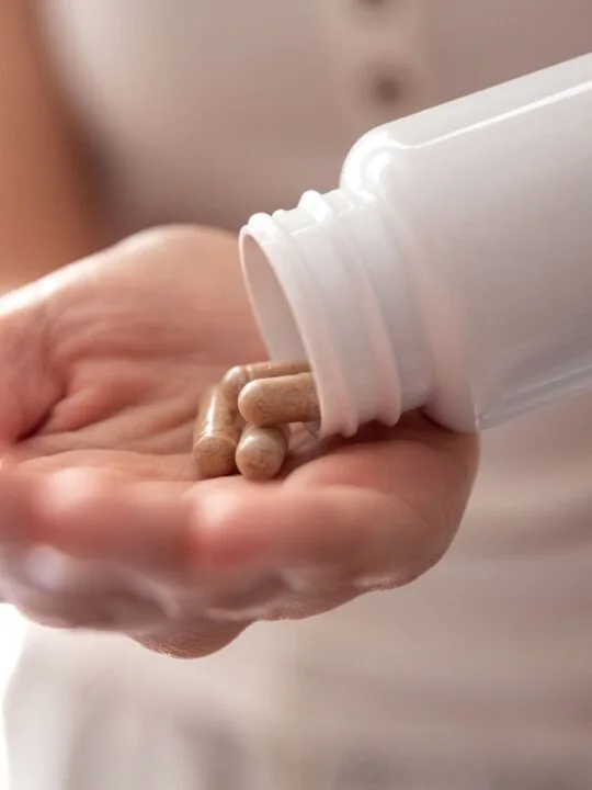 Woman pours tan colored pills from a white pill bottle onto her palm.