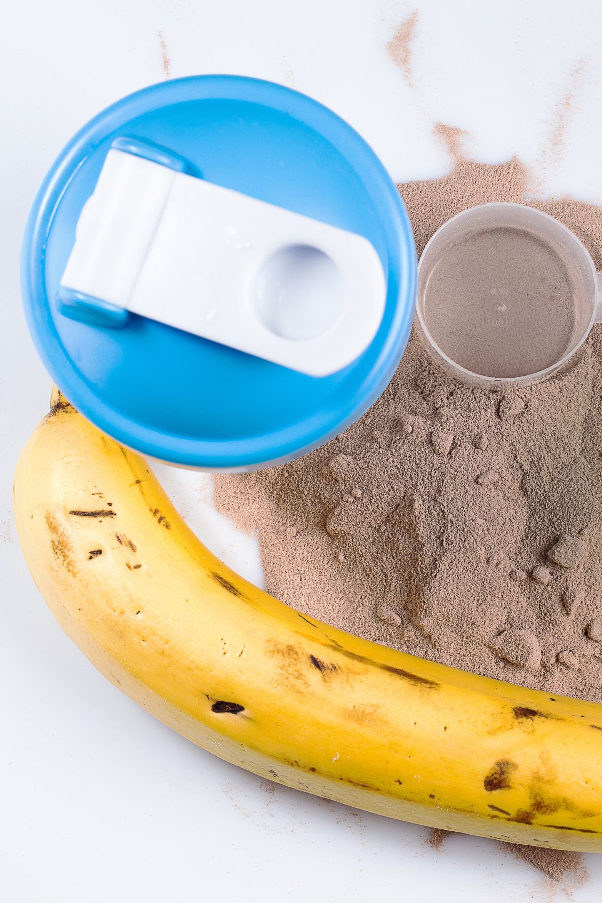 Chocolate protein powder next to a ripe banana and bottle with blue and white cap.