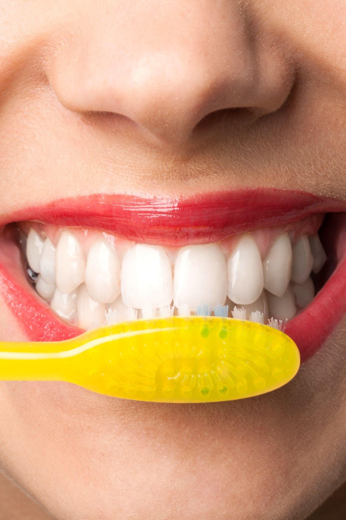 Close up image of a woman brushing her teeth with a yellow toothbrush.