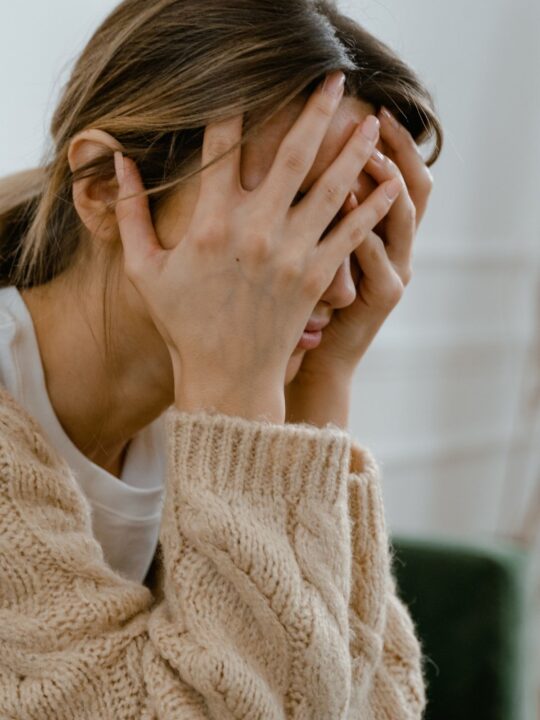 Woman in tan sweater cradles her head in her hands in frustration.