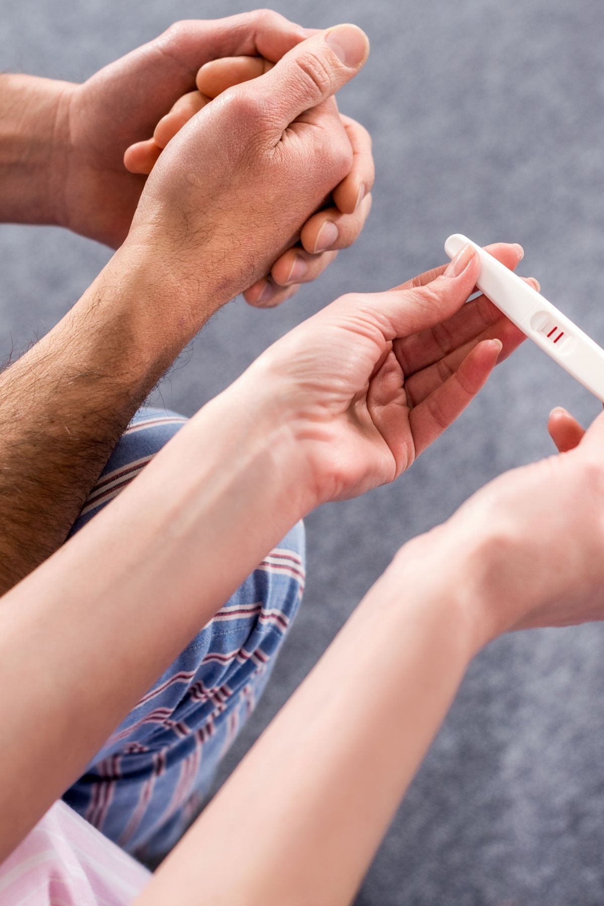 The out-stretched hands of a couple holding a positive home pregnancy test.