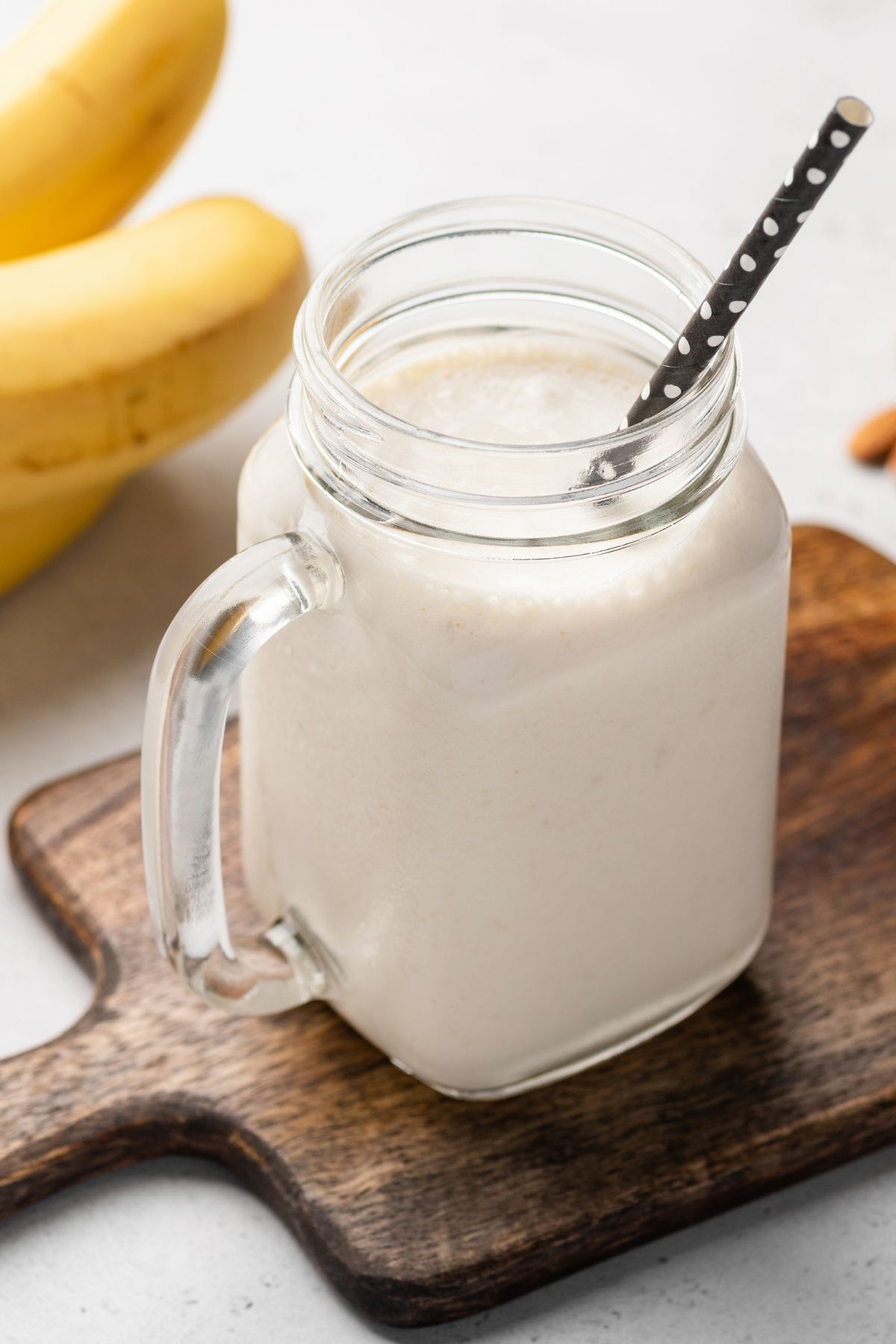 Protein shake in glass mason jar with black straw next to bananas.