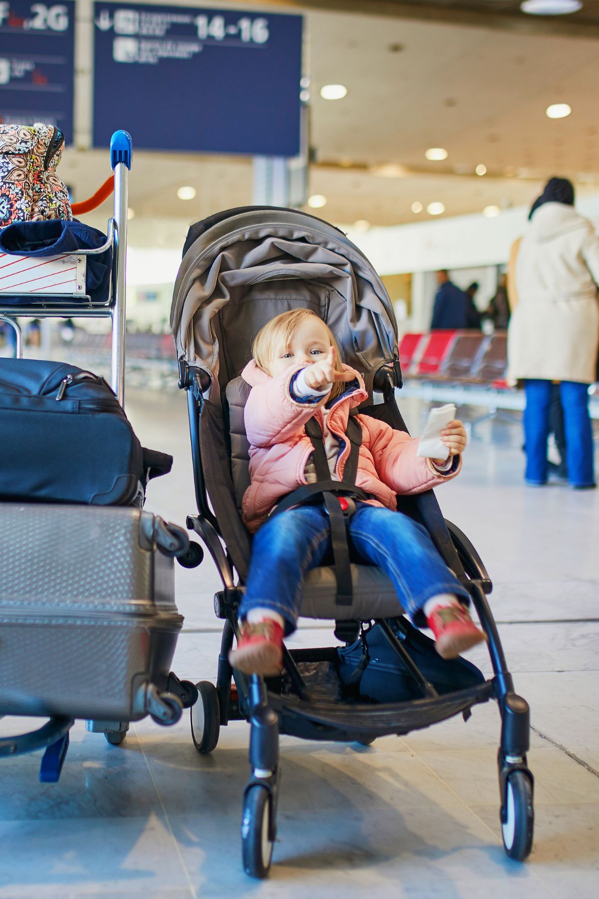 Toddler in a stroller next to cart of luggage in an airport.