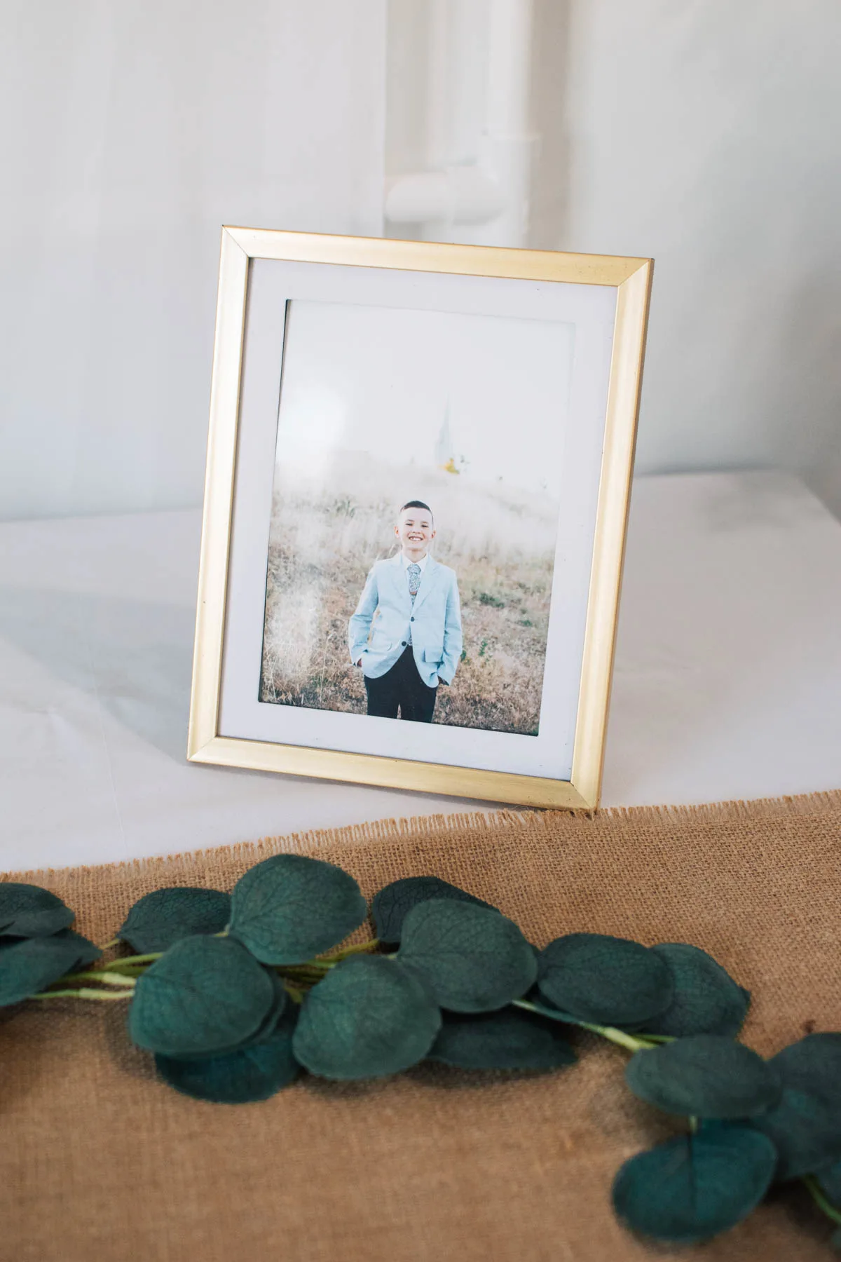 Boy's baptism picture in gold frame on table with garland and runner.
