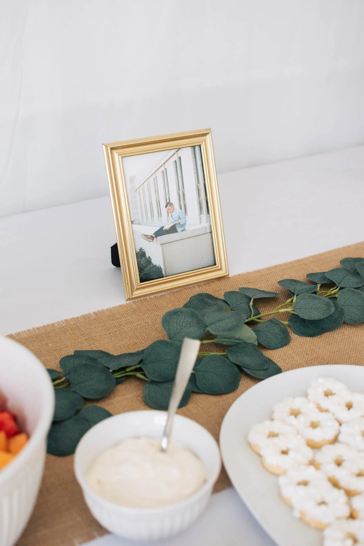 Boy's baptism picture in gold frame on food table with garland and cookie platter.