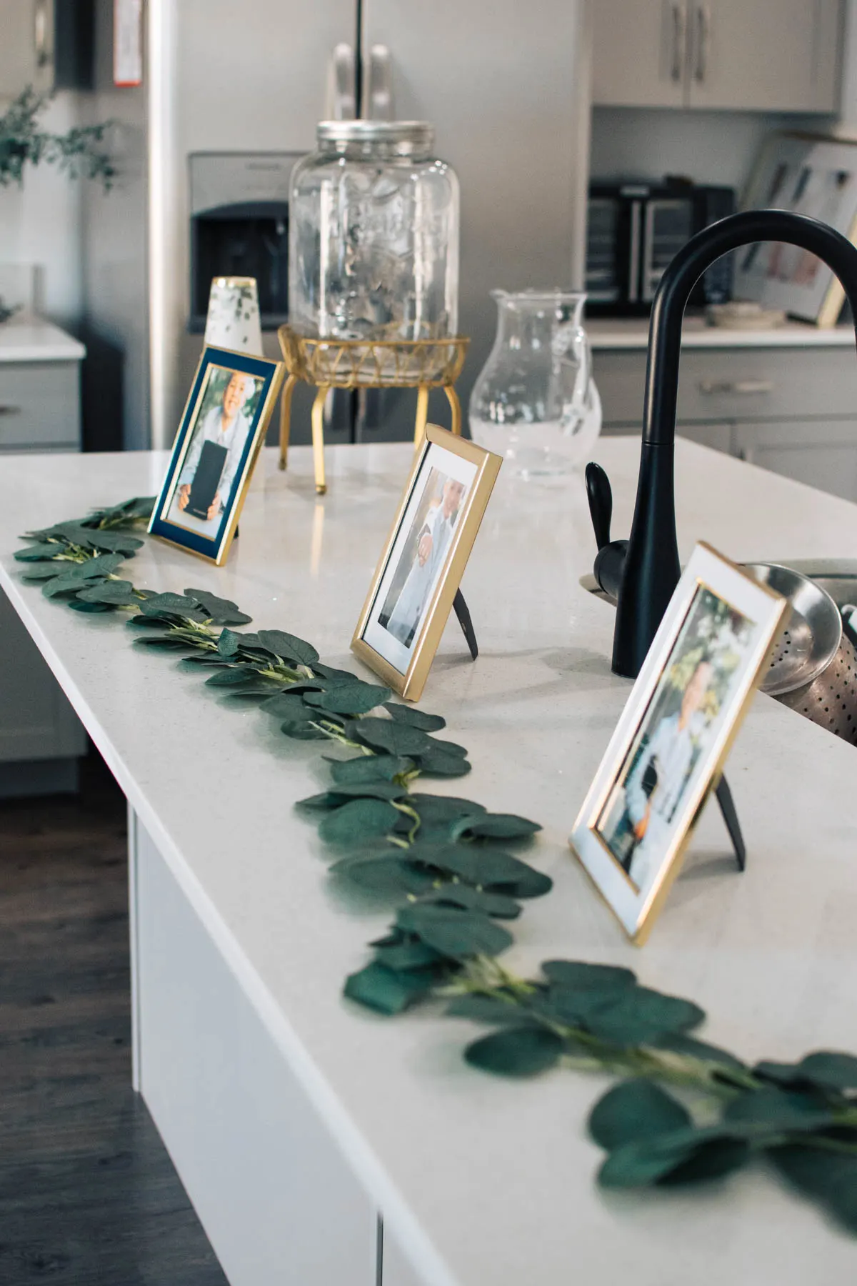 Three baptism picture frames on kitchen counter with eucalyptus garland in front.