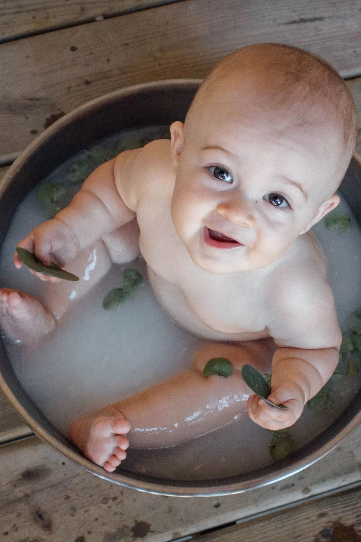 A smiling baby in a small round tub filled with breast milk bath water.