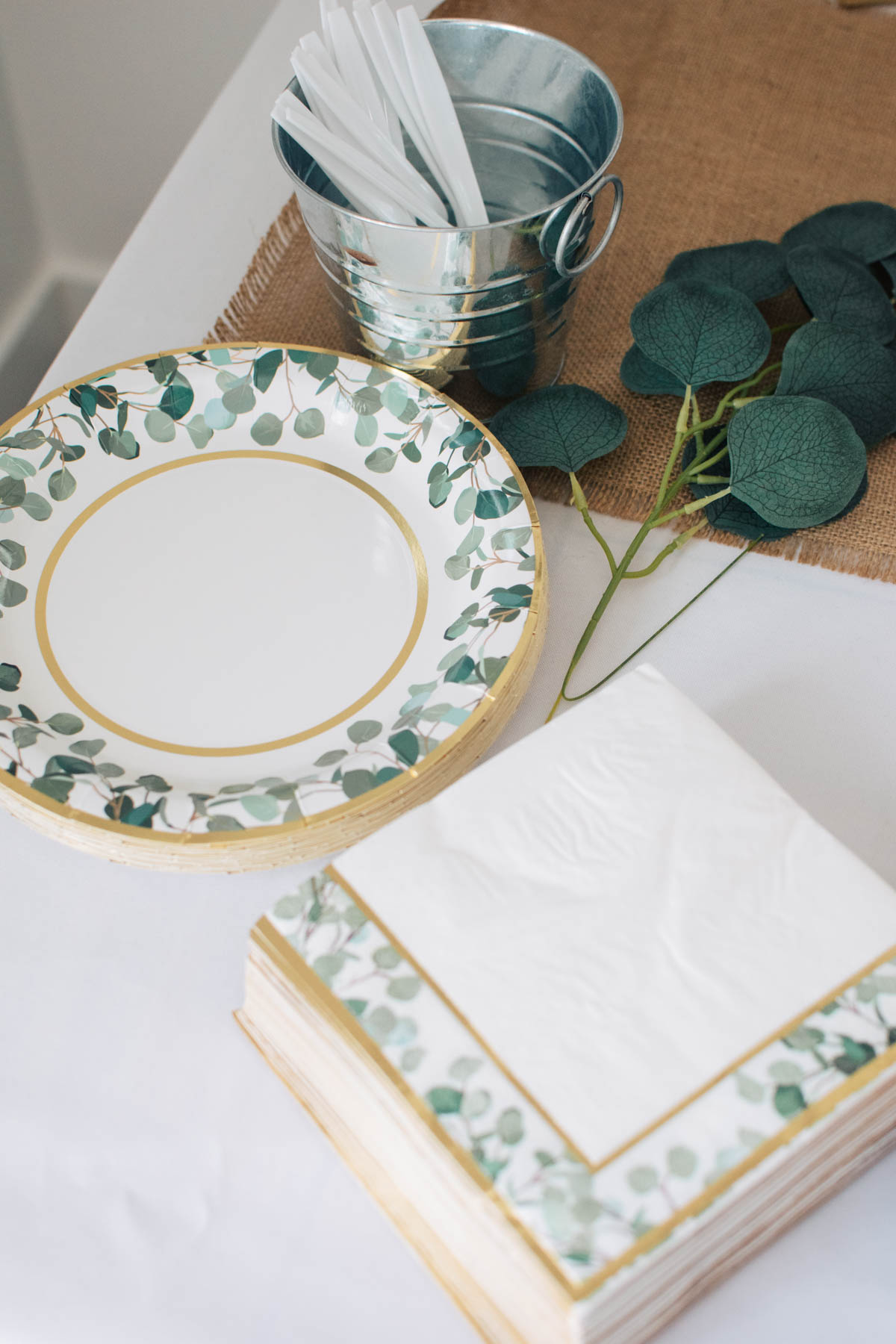 Stack of eucalyptus plates and napkins on table with white table cloth.