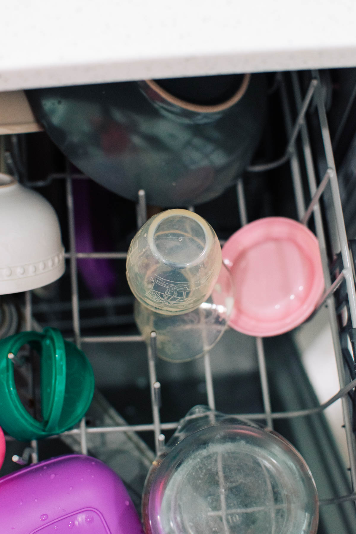 Haakaa pump and pink lid in dishwasher rack surrounded by other dishes.