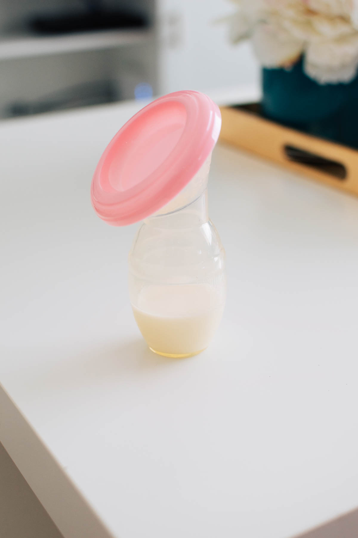 Silicone pump partly full of breast milk and covered with pink lid on white table top.