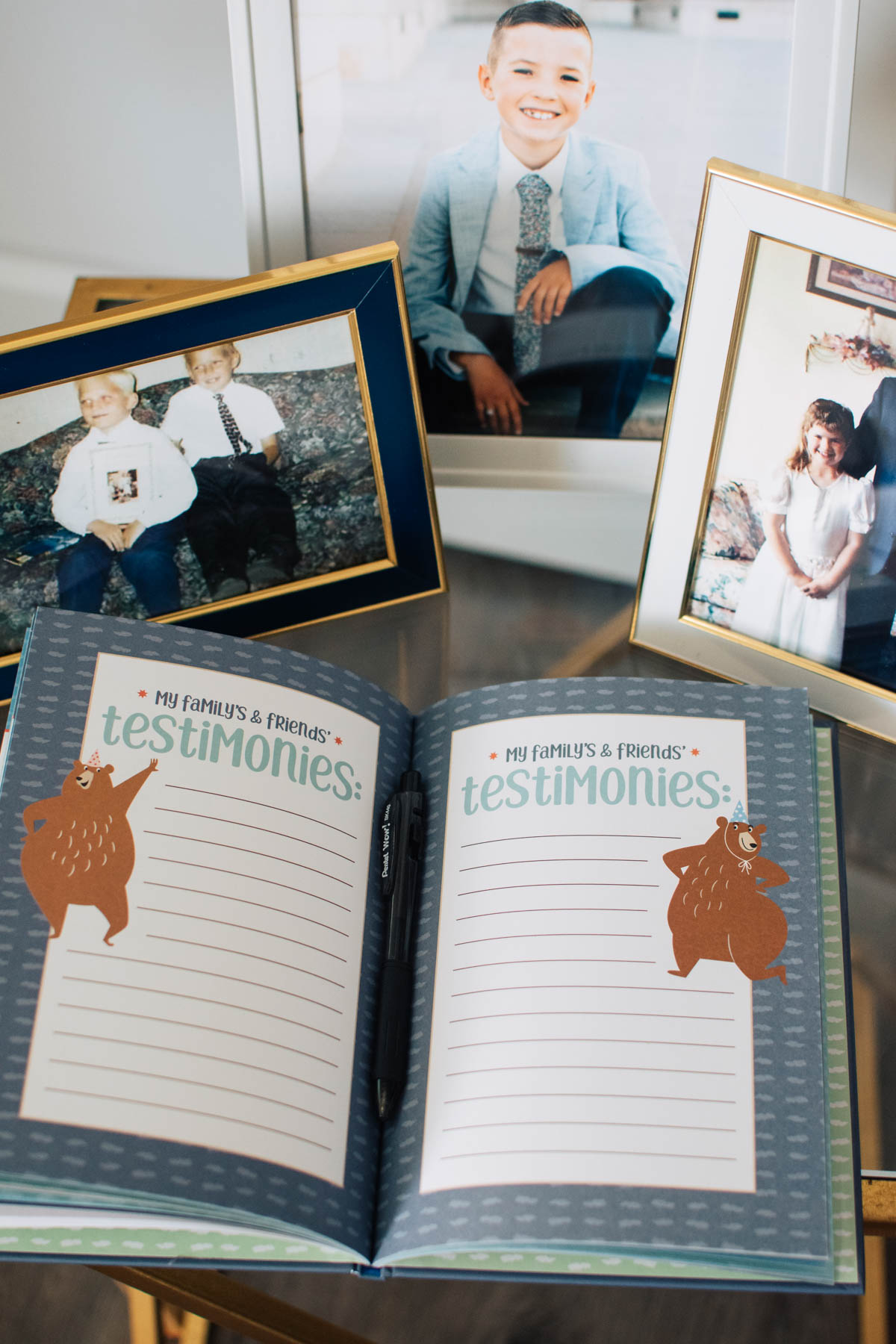LDS baptism testimony book on table with three picture frames surrounding.