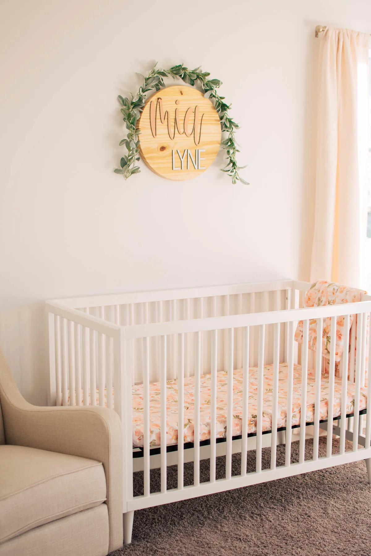White crib with floral crib sheets next to glider rocking chair in nursery.