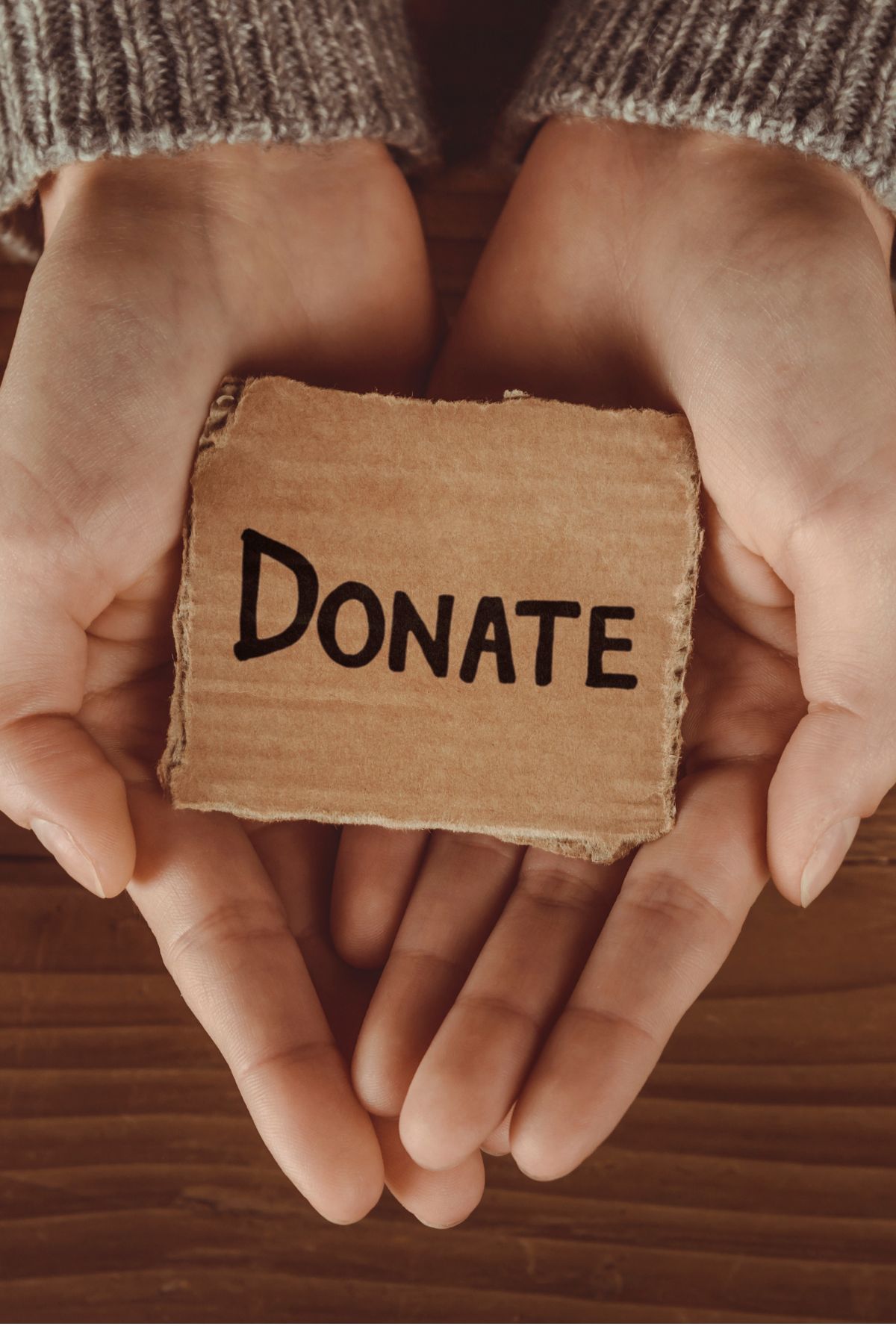 Outstretched hands hold a small cardboard sign with the word donate written in black marker.