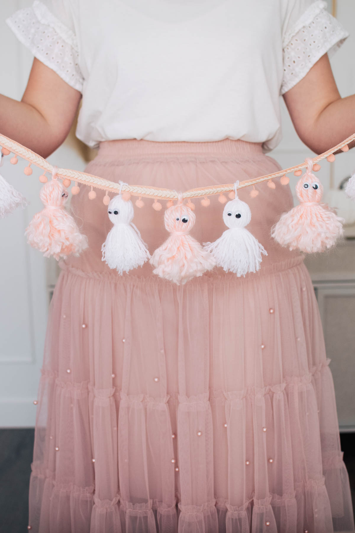 Woman wearing pink skirt holds pink and white yarn ghost garland.