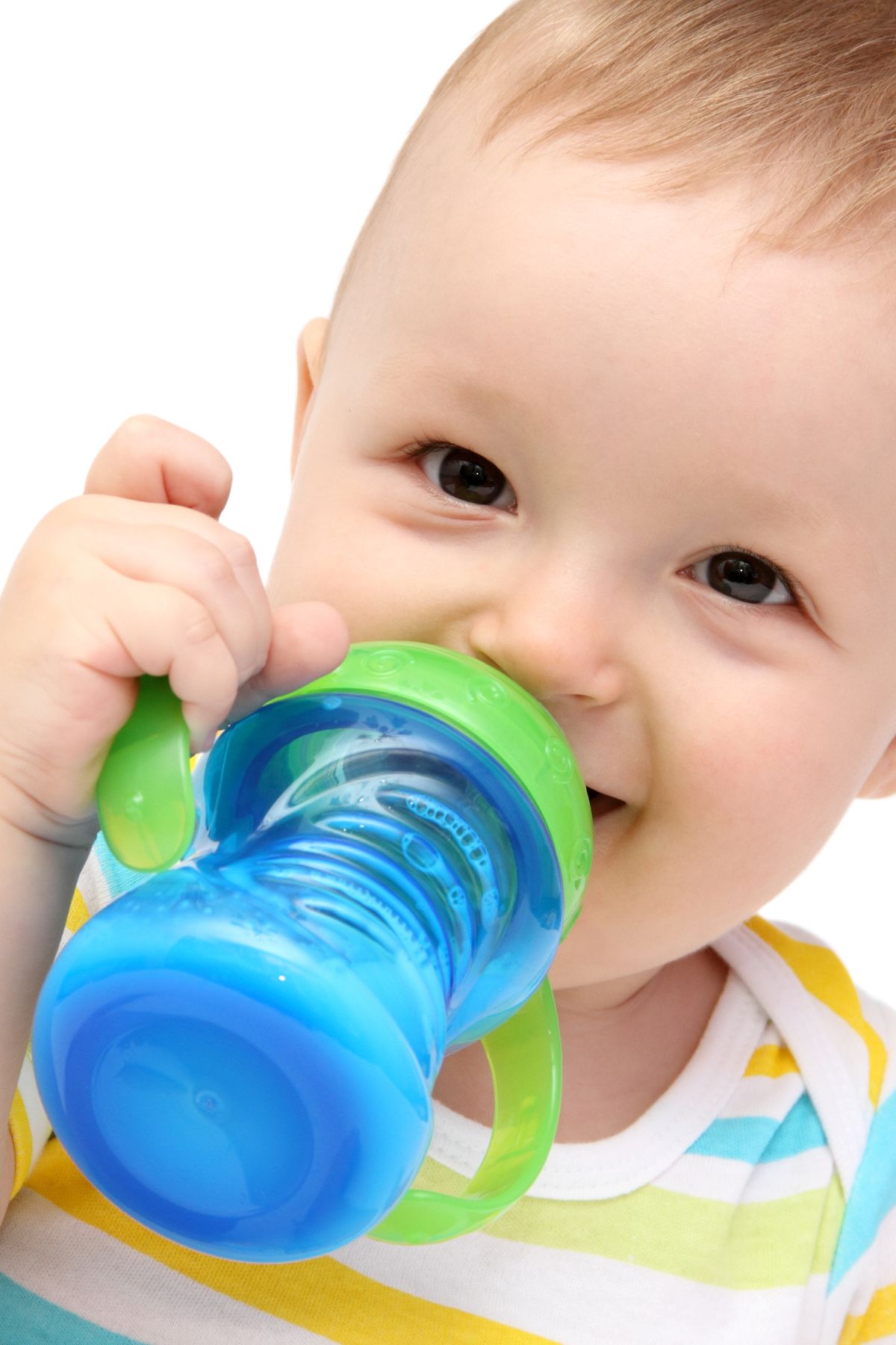 A toddler boy drinks whole milk from a blue and green sippy cup.