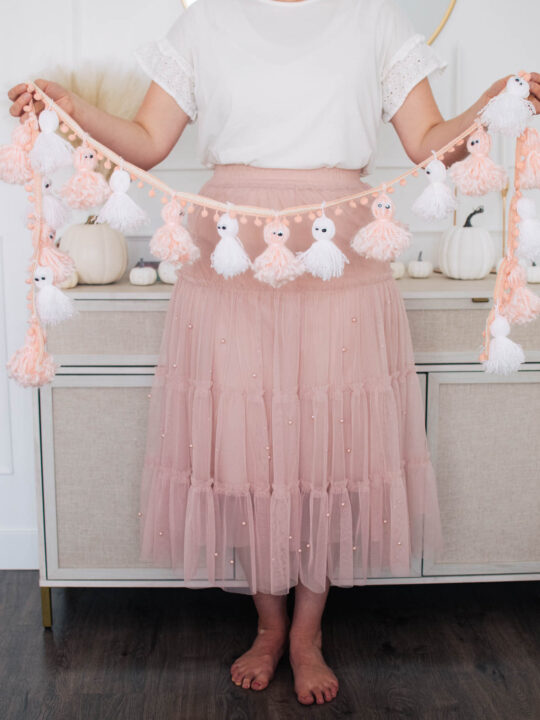 Woman wearing white shirt and pink skirt holds pink and white ghost garland.