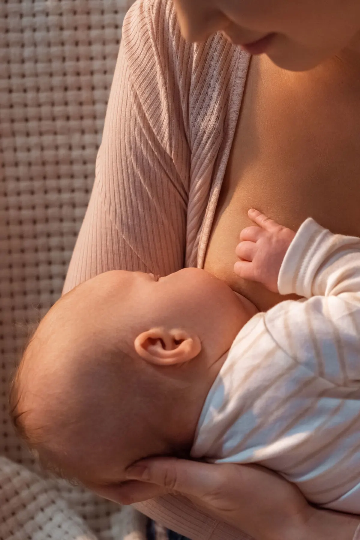 A mom in a pink cardigan breastfeeding her baby girl in a dimly lit room.
