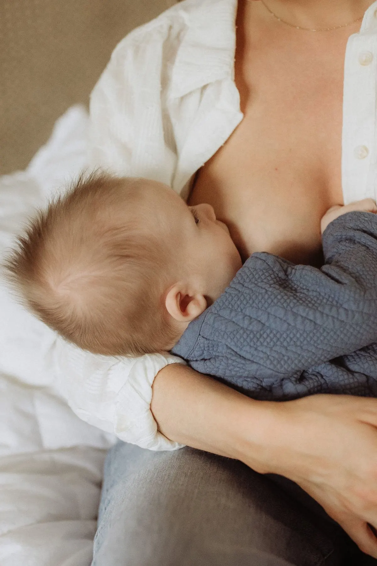Torso shot of a woman breastfeeding a baby boy in blue shirt.
