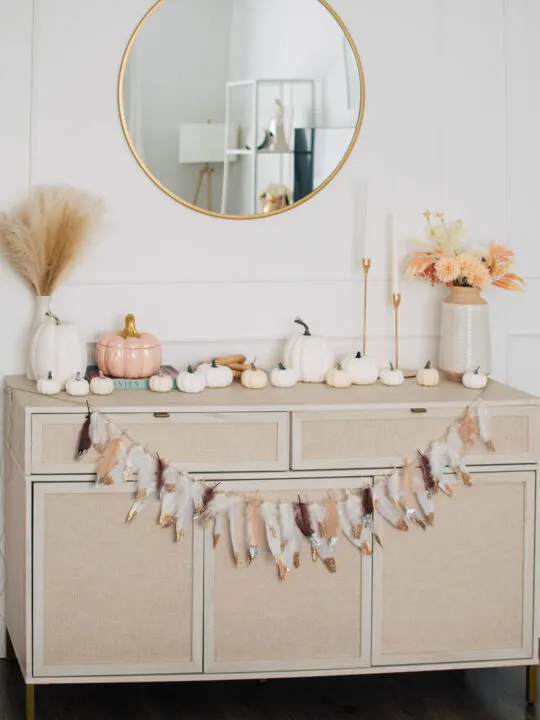DIY fall garland made of feathers on cream colored sideboard.
