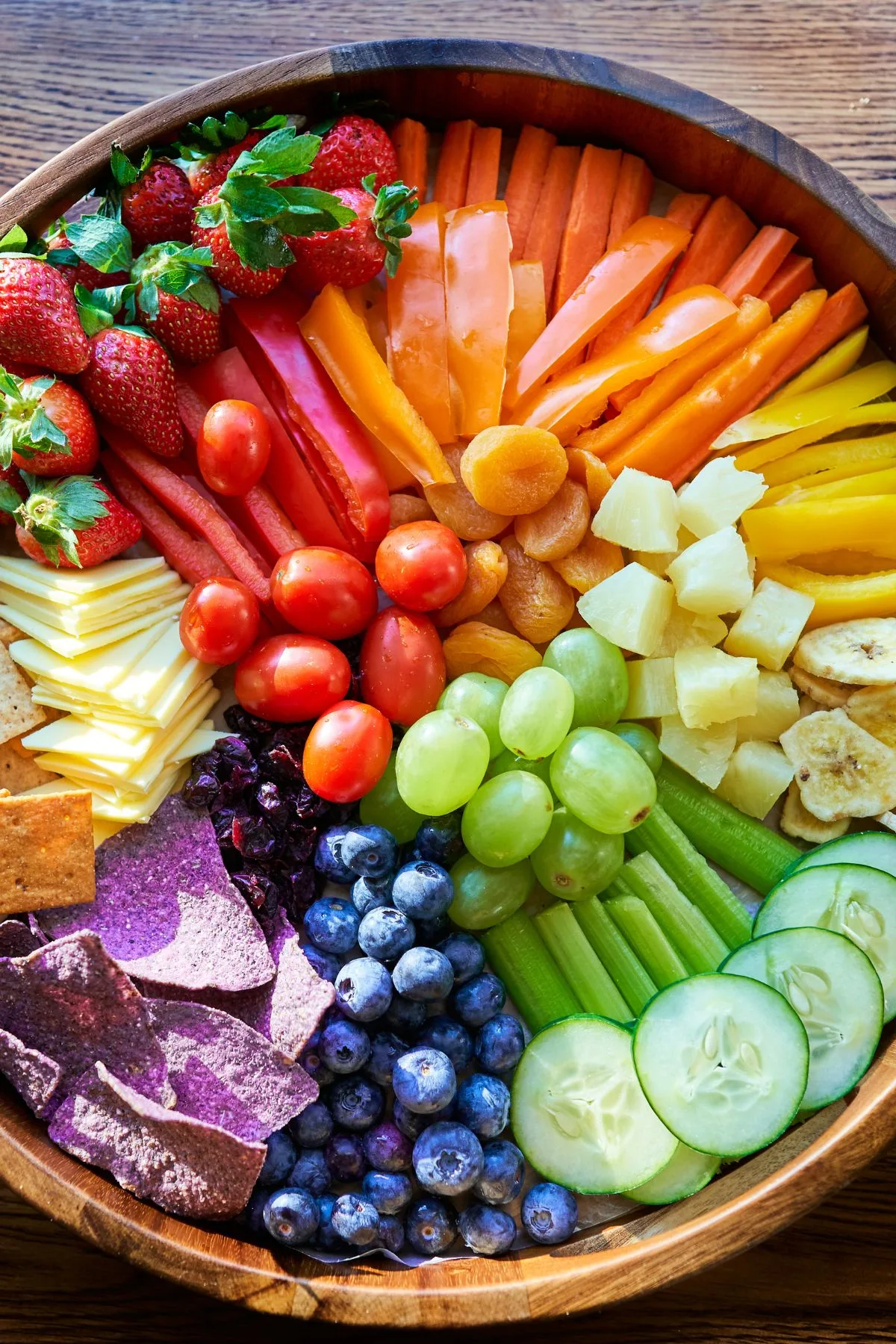 A large platter filled with fruits and vegetables like tomatoes, blueberries, carrots, and grapes.
