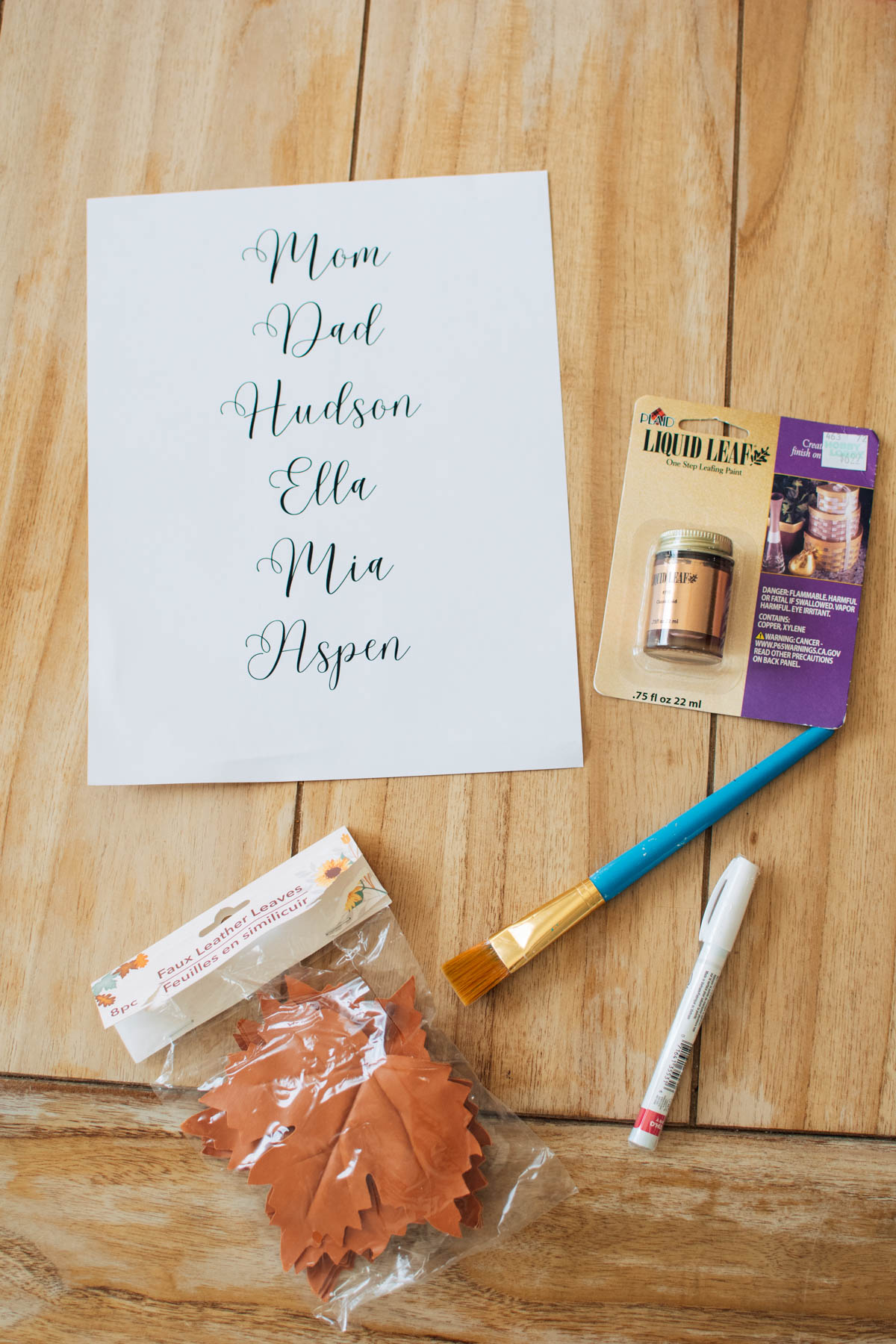 DIY leaf place card supplies on table including liquid leaf, paintbrush, and marker.