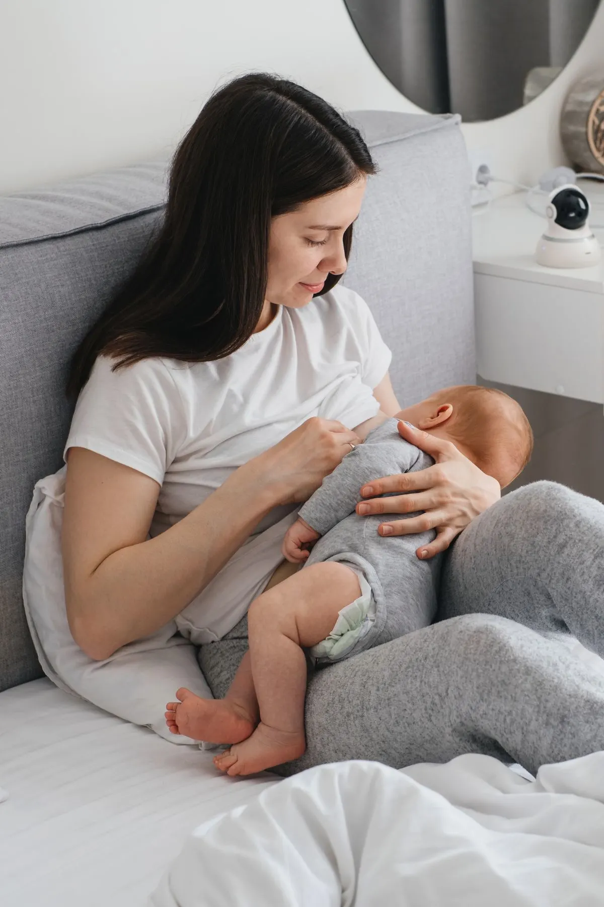 A sick woman breastfeeding her baby while sitting in bed.