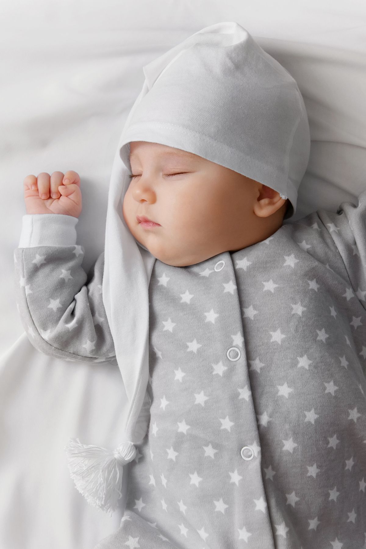 A baby sleeping in gray and white pajamas with a matching sleep cap.