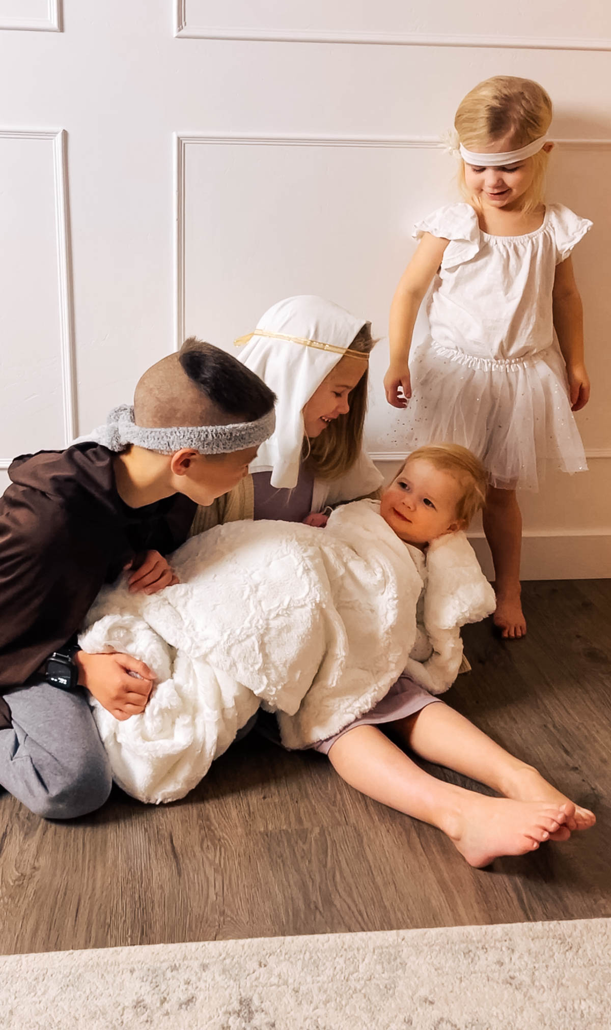 Four children dressed in costumes act out the nativity scene in a living room.