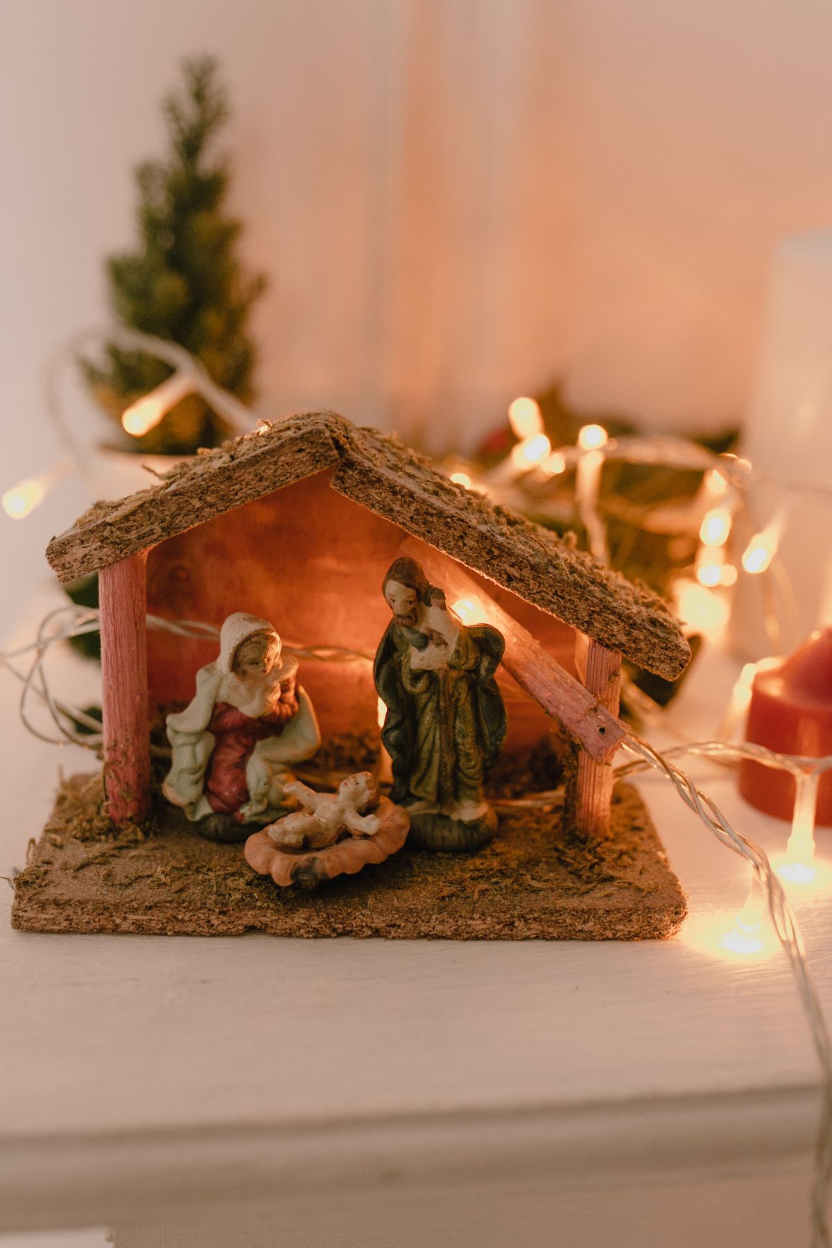 A a small nativity scene on a table with Christmas lights in the background.