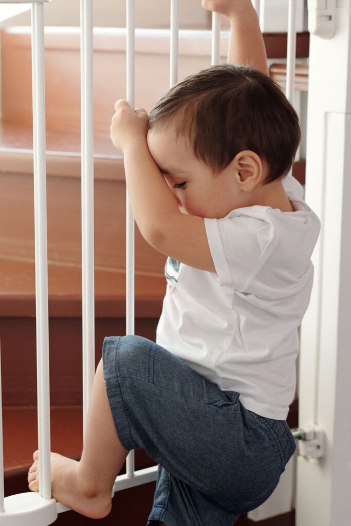Toddler boy climbs on the rails of a hardware-mounted baby gate.