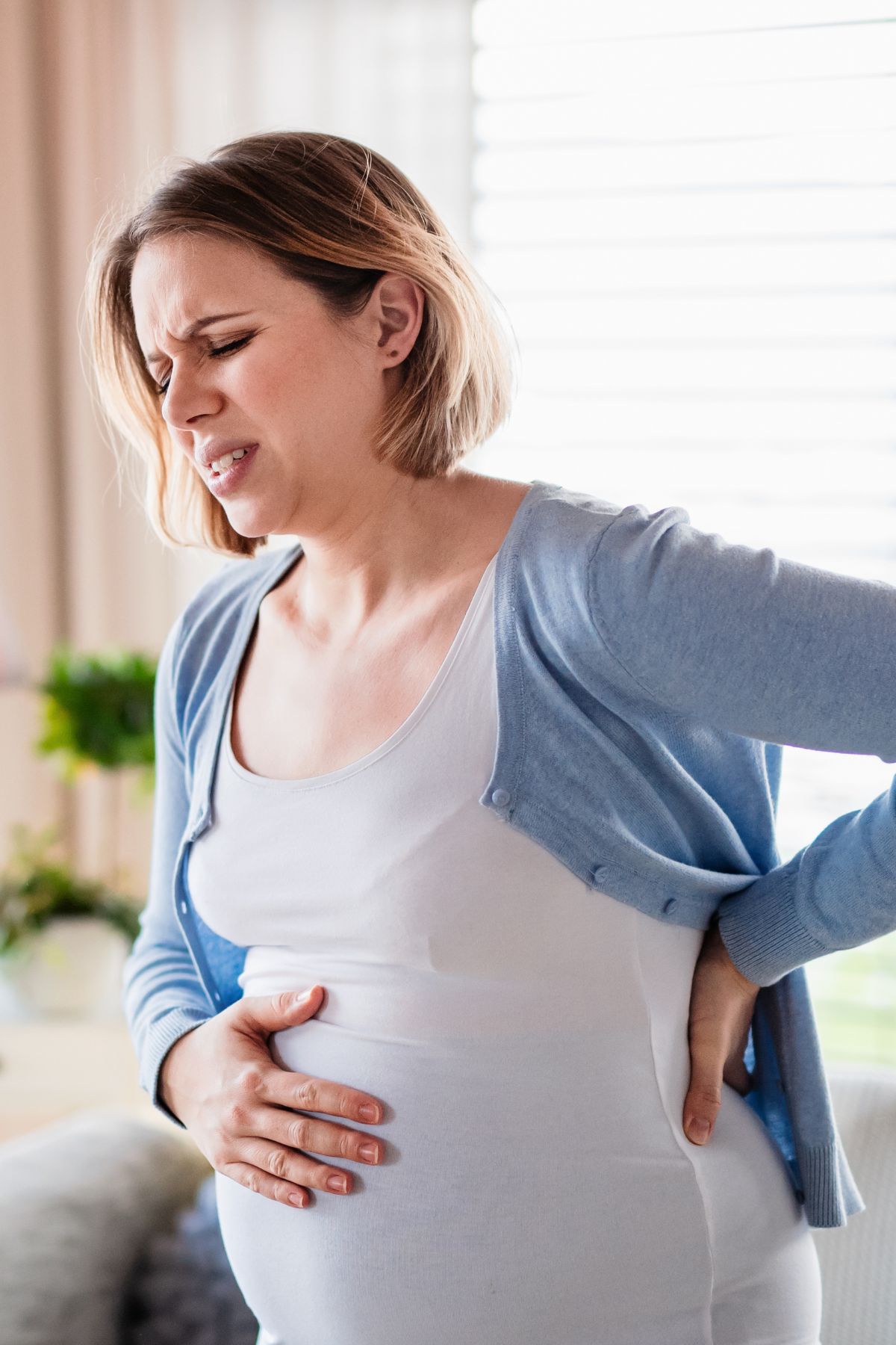 A pregnant woman hunches over in pain with a hand on her lower back and belly.