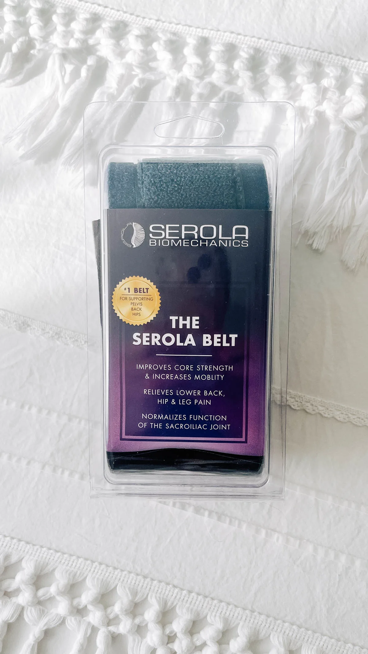 The Serola pelvic support belt in its packaging on a white bedspread.