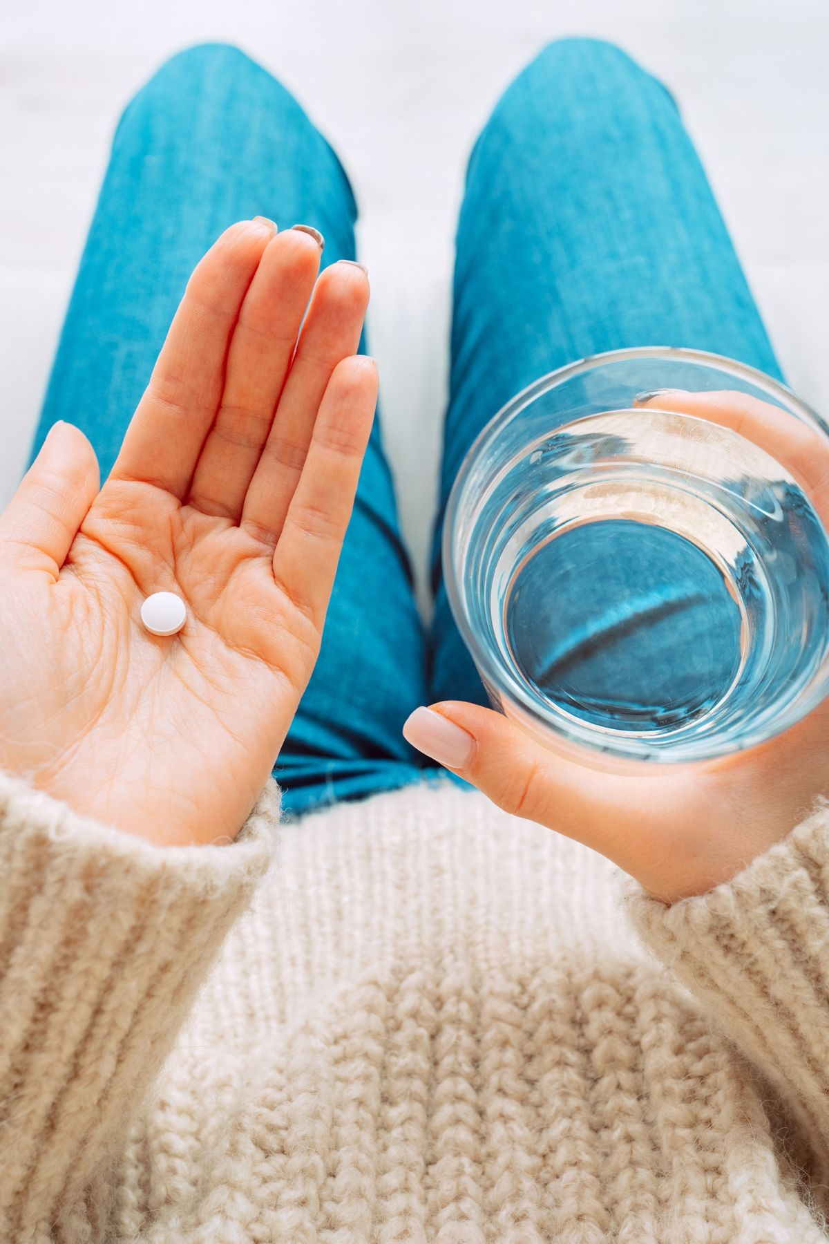 A woman holds a Midol pill in one hand and a glass of water in the other.