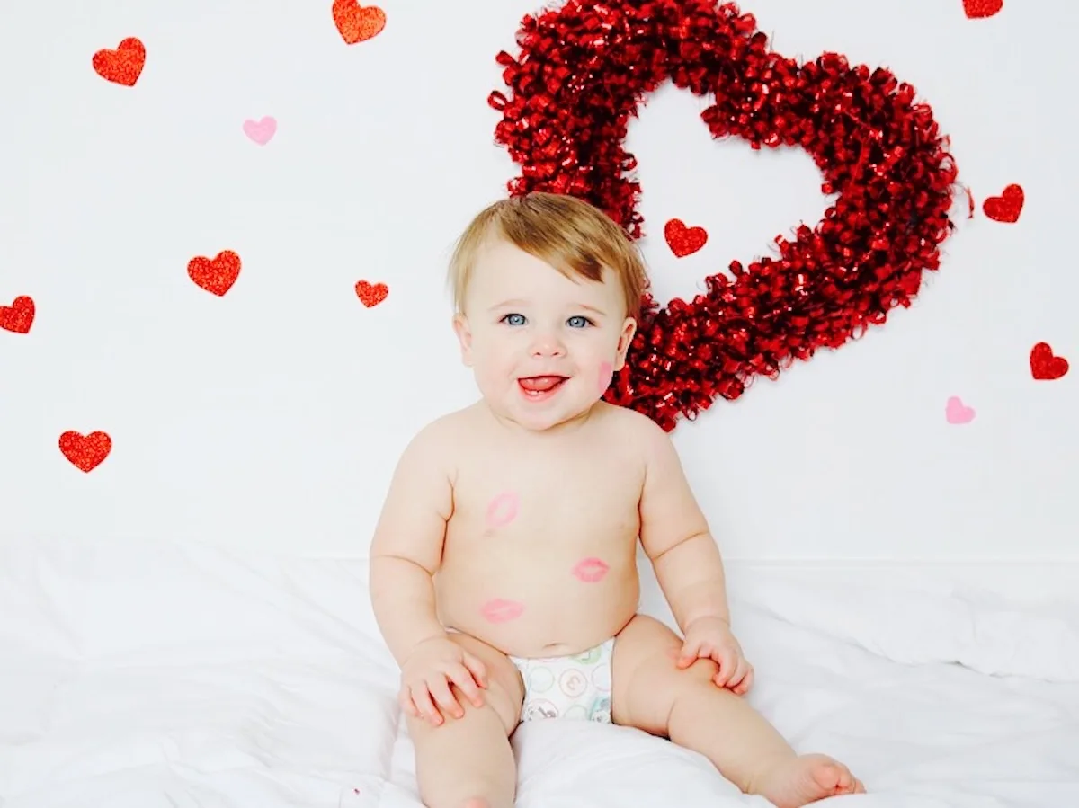 A baby boy poses in front of a white background with various sized hearts.