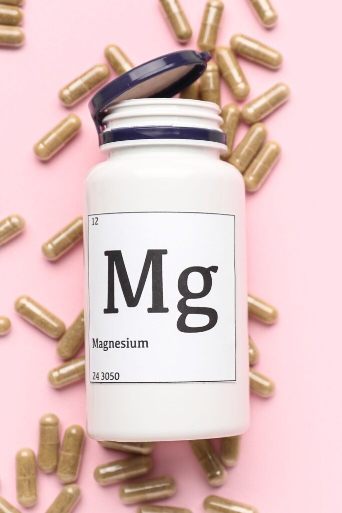 Bottle of magnesium supplements surrounded by pills on a pink background.
