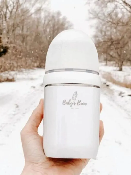 A woman holds up a baby's brew bottle warmer outside with a snowy background.