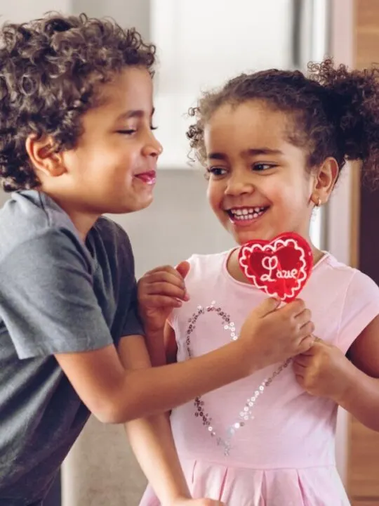 Smiling siblings hold a Valentine's Day sucker shaped like a heart.