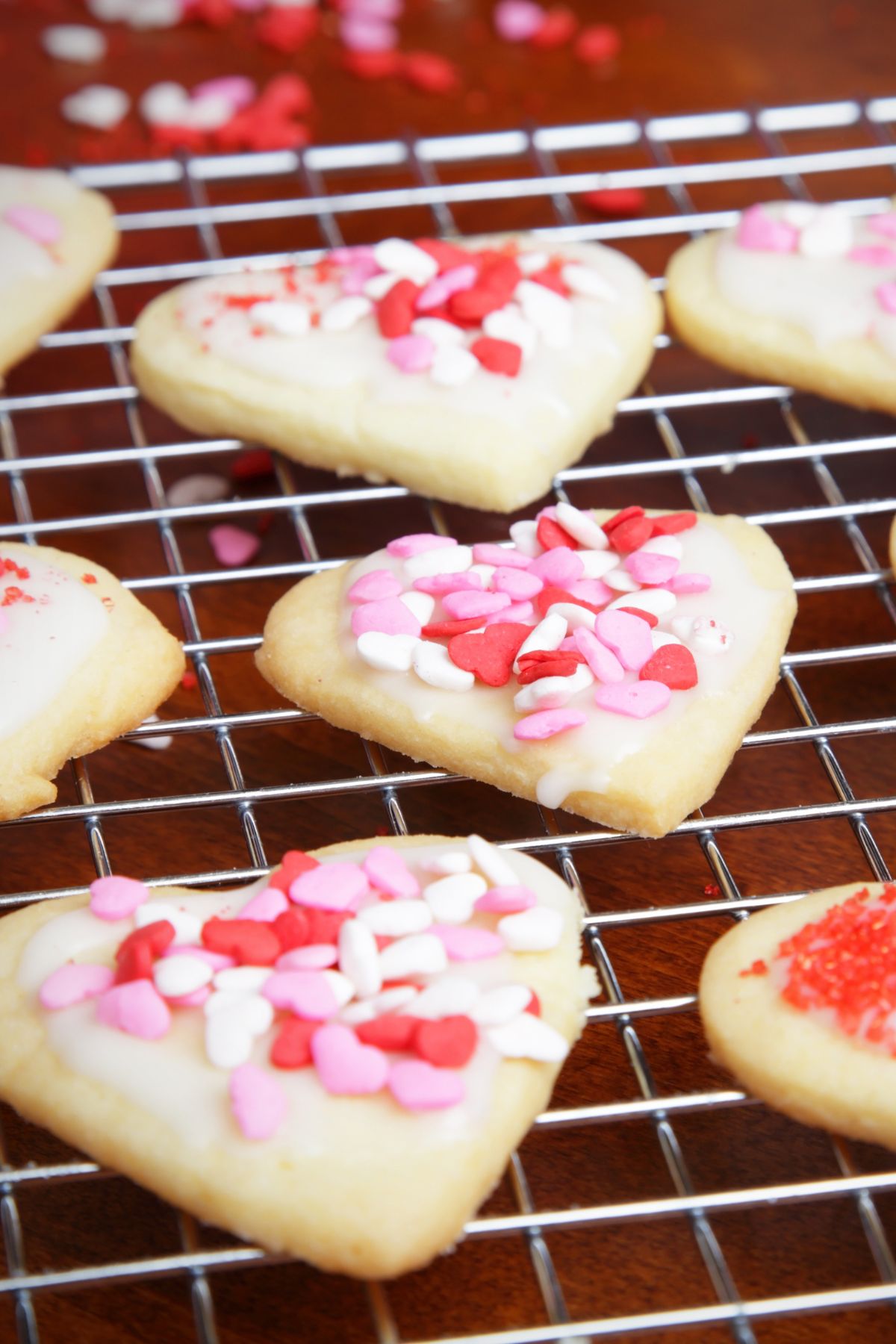 Heart-shaped cookies on a cooling rack with pink and red sprinkles.
