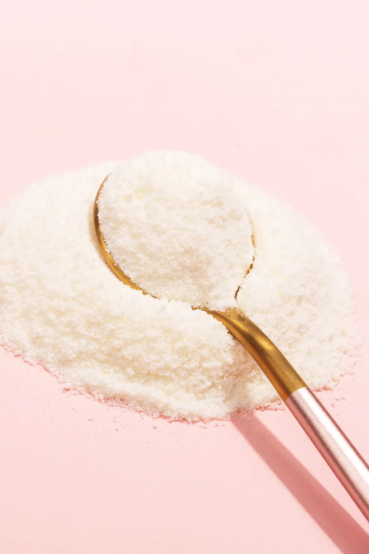 Pile of white magnesium powder with a gold spoon on a pink background.