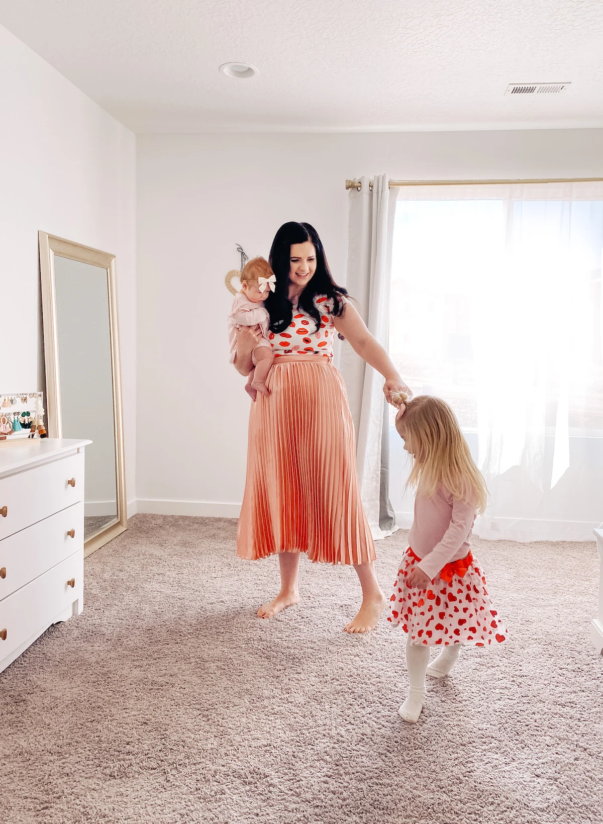 A mom dances with her daughters while wearing coordinating outfits for Valentine's Day.